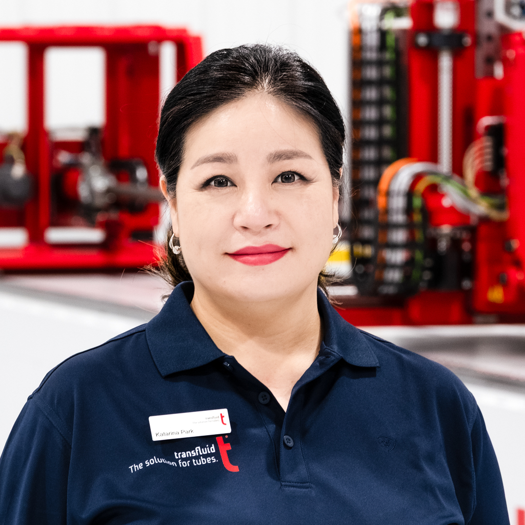 Mitarbeiterin im blauen Firmenpoloshirt mit Namensschild vor Industrieanlage.