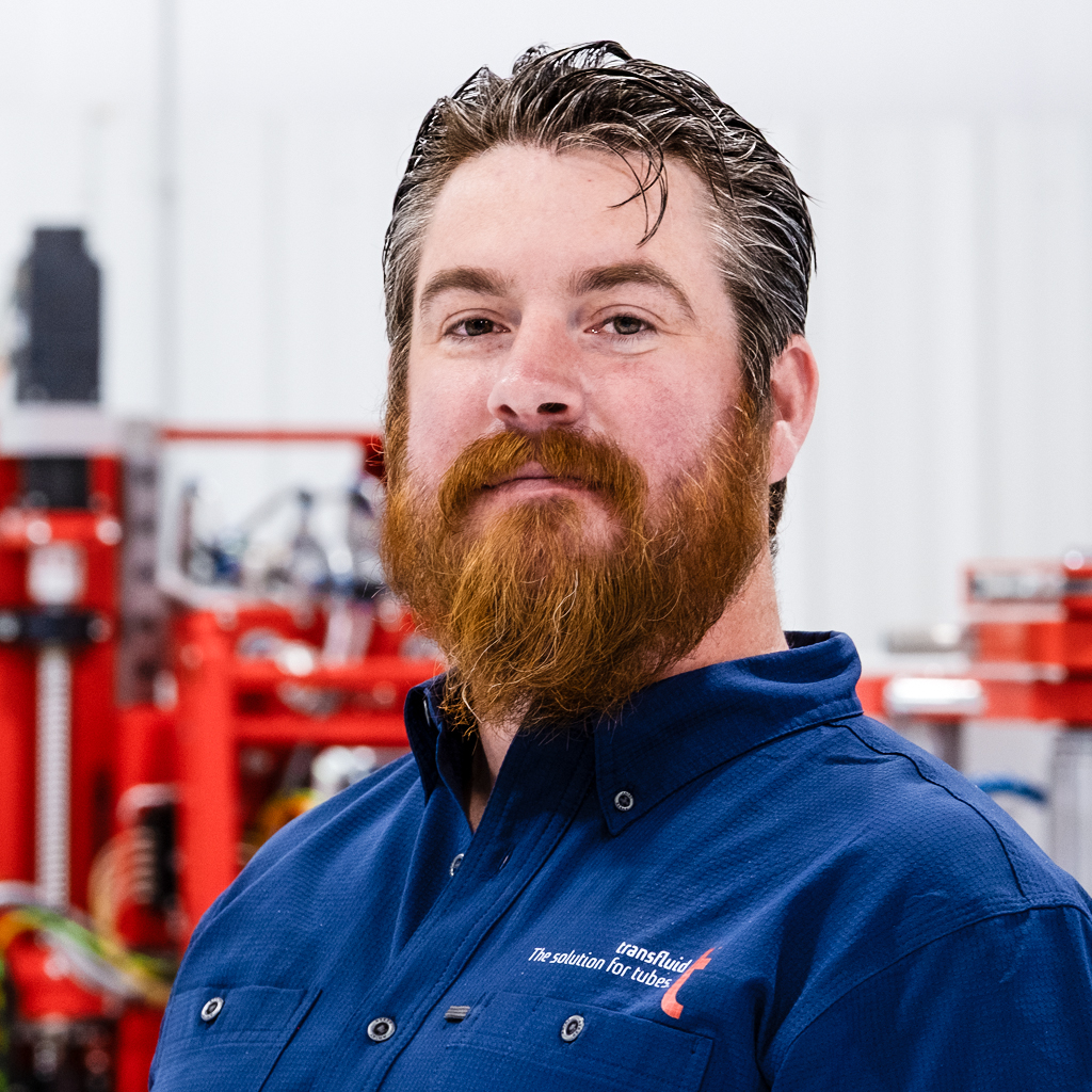 Mitarbeiter mit rotem Bart im blauen Firmenhemd vor Industrieanlage.