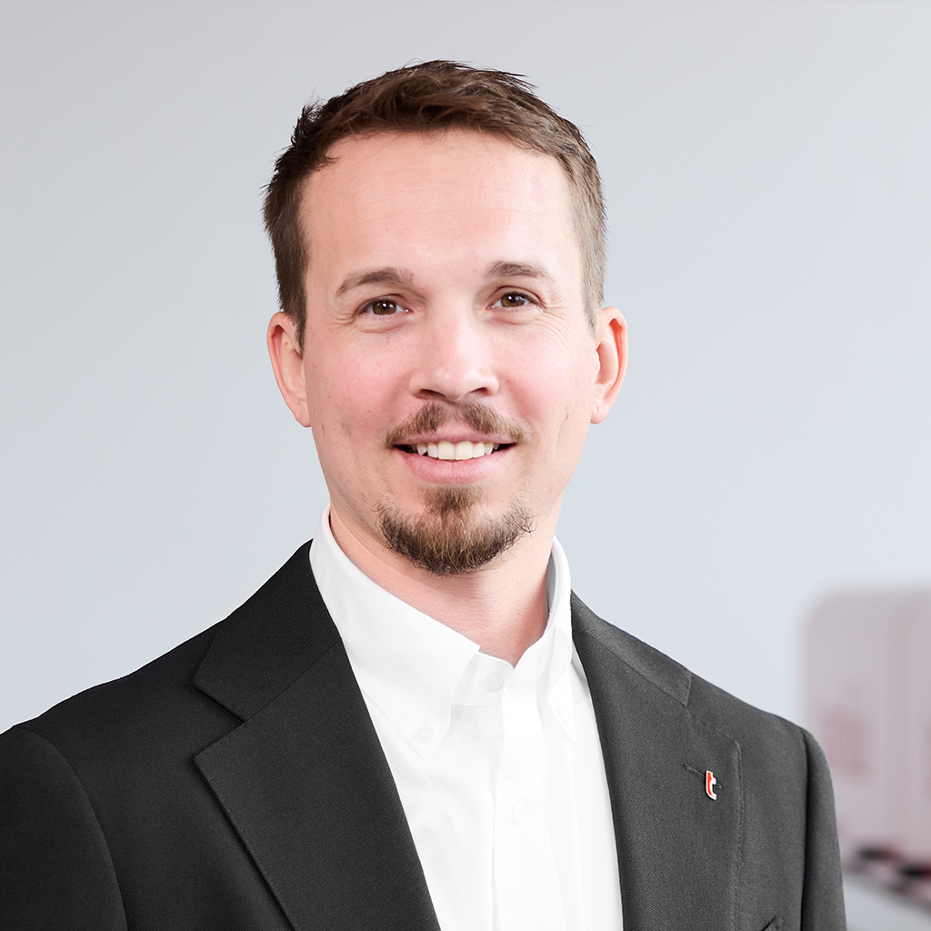 Mitarbeiter im weißen Firmenhemd mit Kinnbart vor Industrieanlage.