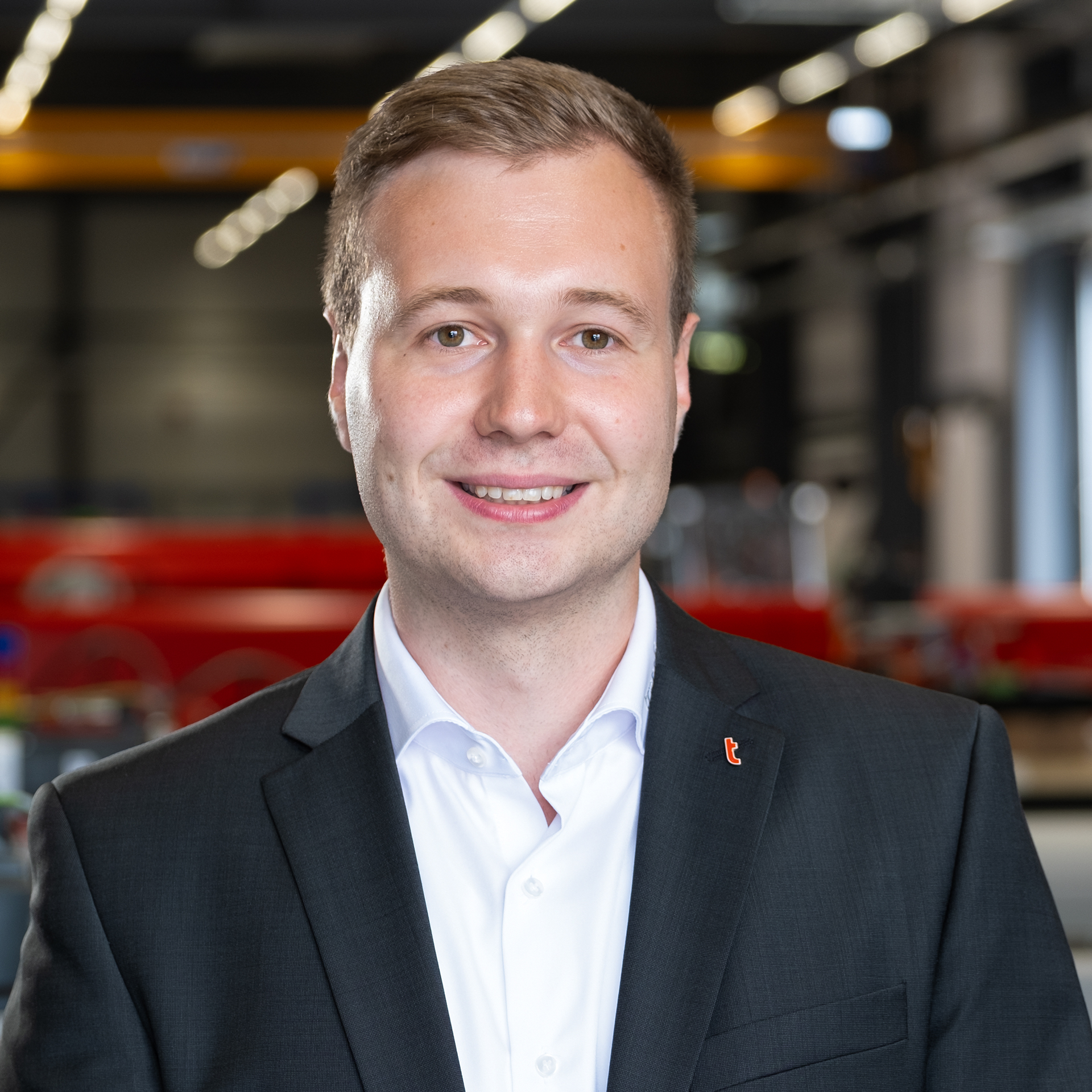 Mitarbeiter im Anzug in moderner Industriehalle mit Maschinen im Hintergrund.