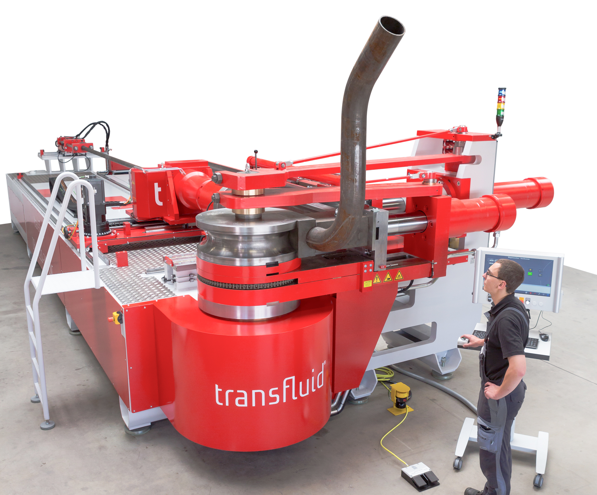 CNC-Dornbiegemaschine von transfluid mit Bediener am Steuerpult beim Biegen eines großen Stahlrohrs in einer industriellen Fertigungsumgebung.