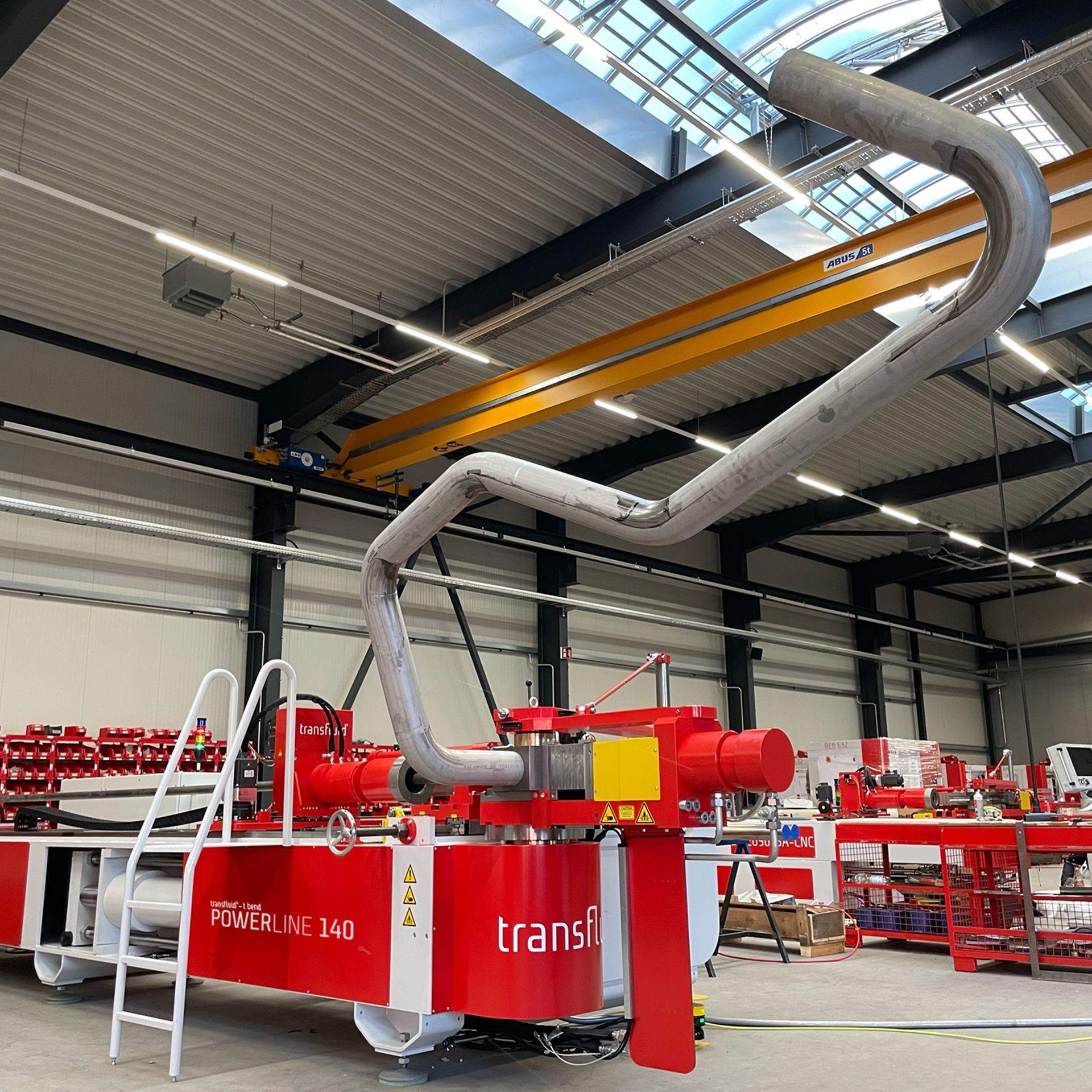CNC-Dornbiegemaschine t bend POWERLINE 140 von transfluid beim Biegen eines großen Metallrohrs in einer industriellen Produktionshalle.