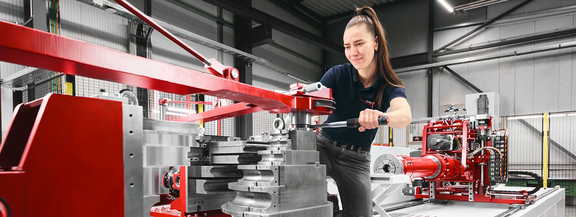 Mitarbeiterin bedient transfluid Rohrbiegemaschine in moderner Produktionshalle.